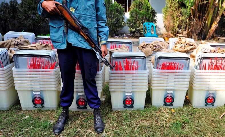 A member of the police stands guard in front of ballot boxes at a distribution centre ahead of parliamentary elections in Dhaka